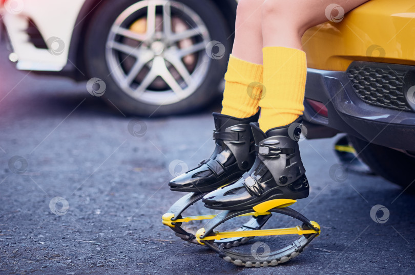 Скачать Ботинки Kangoo Jump на ногах спортивной девушки, сидящей на бампере желтого спортивного автомобиля. фотосток Ozero