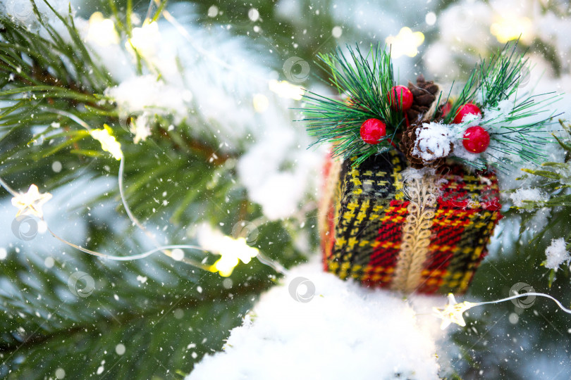 Скачать Рождественская подарочная коробка на ветке натуральной ели, покрытой снегом. Новый год на открытом воздухе. Снегопад, огни гирлянд, праздничное настроение сказки и волшебства, уличное убранство. Пространство для копирования фотосток Ozero