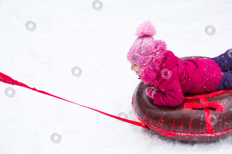 Скачать Девушка катается на тюбике с горки зимой в снегопад. Тюбинг, зимние виды спорта на открытом воздухе и семейные развлечения. Теплая одежда, вязаная шапочка с помпоном. фотосток Ozero