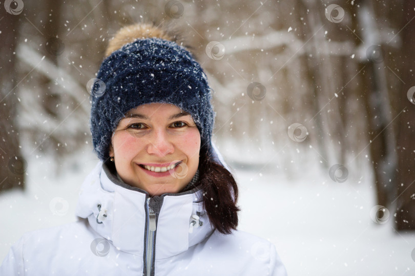 Скачать Женщина в теплой вязаной шапке, надвинутой на глаза, улыбается и наслаждается снегом, холодной погодой. Мероприятия на свежем воздухе, сезон, зима, тает снег. Покрытая инеем, прекрасная улыбка. Портрет крупным планом фотосток Ozero