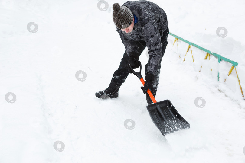Скачать Мужчина убирает снег лопатой зимой на подметенном дворе после снегопада. Зимние погодные условия, лопата для уборки снега в багажник автомобиля фотосток Ozero