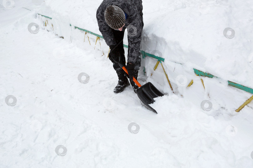 Скачать Мужчина убирает снег лопатой зимой на подметенном дворе после снегопада. Зимние погодные условия, лопата для уборки снега в багажник автомобиля фотосток Ozero