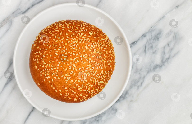 Скачать Свежеиспеченная домашняя булочка с кунжутом для гамбургера или чизбургера крупным планом на белой тарелке на мраморном фоне. Выборочный фокус, вид сверху и пространство для копирования фотосток Ozero