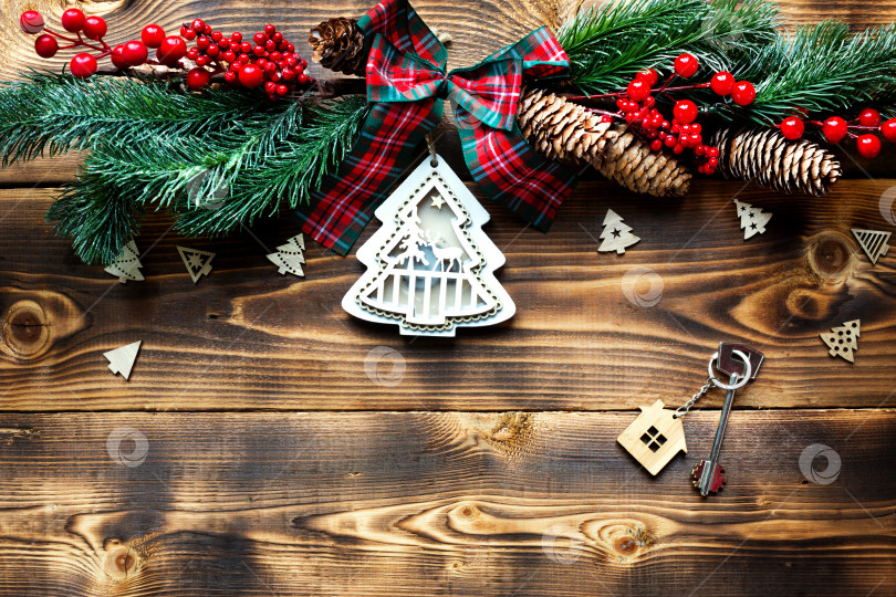 Скачать Ключ от дома с брелком коттедж на праздничном экологически чистом, естественном фоне с рождественской елкой. С Новым годом-красный фон, подарок, поздравительная открытка. Покупка, строительство, переезд, ипотека фотосток Ozero
