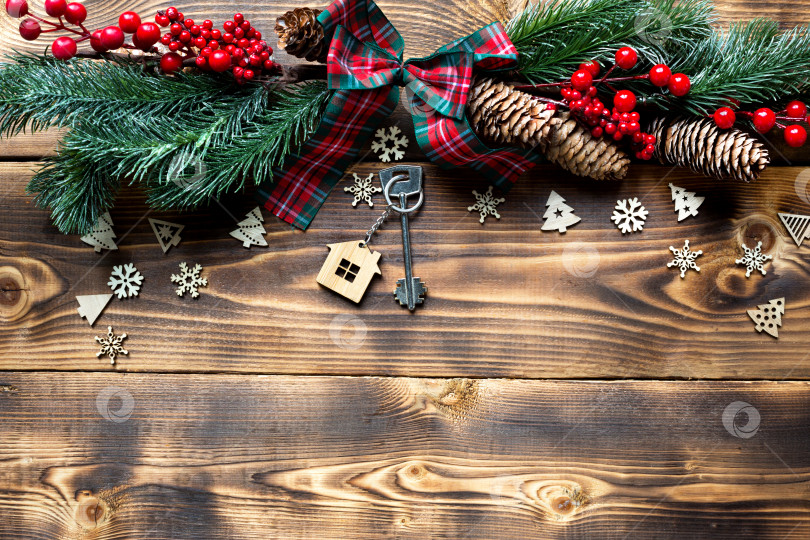 Скачать Ключ от дома с брелком для ключей коттедж на праздничном экологичном, естественном фоне с рождественской елкой. С Новым годом-красный фон, подарок, поздравительная открытка. Покупка, строительство, переезд, ипотека фотосток Ozero