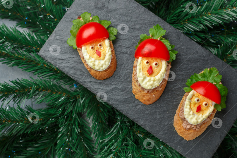 Скачать Новогодние и рождественские бутерброды в виде Деда Мороза из багета с печенью трески или минтая, петрушкой, яйцами и свежими помидорами под майонезом. Вкусная праздничная закуска для вечеринки фотосток Ozero