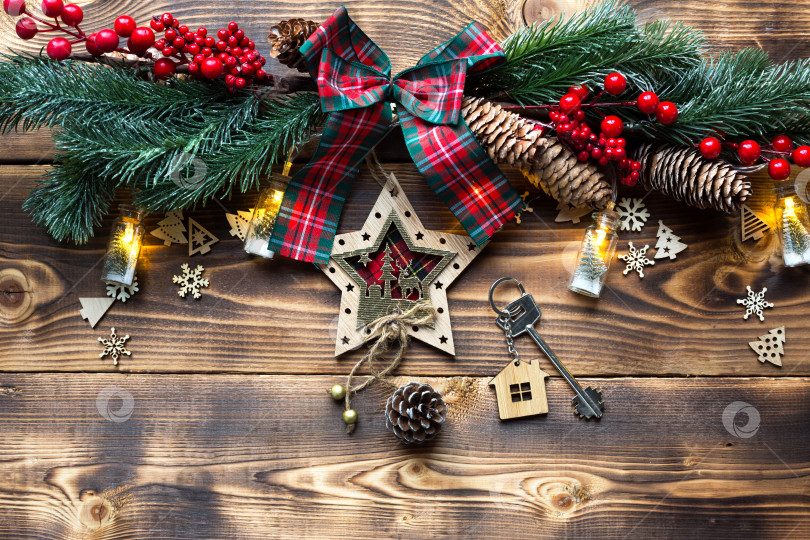 Скачать Ключ от дома с брелком коттедж на праздничном экологически чистом, естественном фоне с рождественской елкой. С Новым годом-красный фон, подарок, поздравительная открытка. Покупка, строительство, переезд, ипотека фотосток Ozero