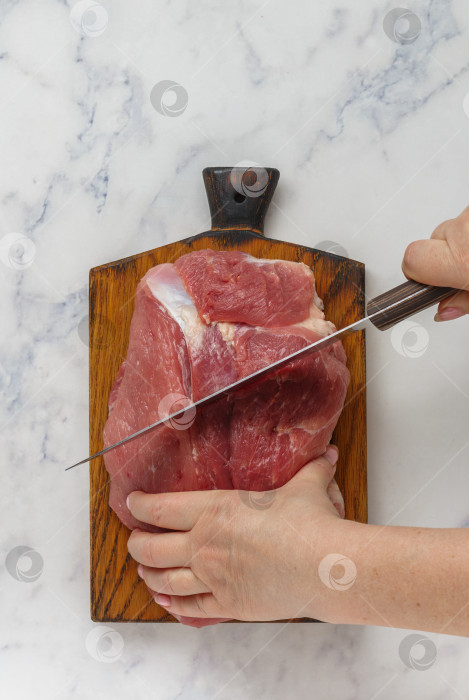 Скачать Женские руки нарезают органическое сырое свиное мясо на разделочной доске на мраморном фоне. Концепция приготовления домашней еды.   выборочный фокус, вид сверху, пространство для копирования фотосток Ozero