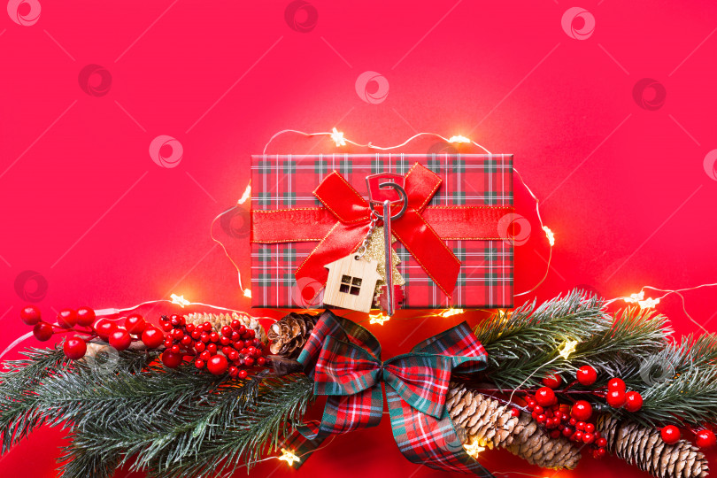 Скачать Ключ от дома с брелком коттедж на праздничном фоне с рождественской елкой, огнями гирлянд. С Новым годом-красный фон, подарок, поздравительная открытка. Покупка, строительство, переезд, ипотека фотосток Ozero