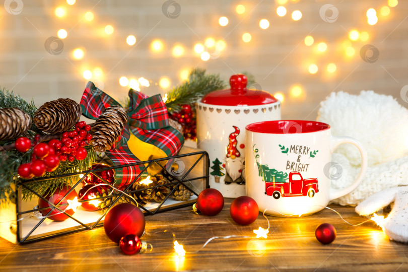 Скачать Рождественская красная кружка с надписью Merry and Bright и банка для печенья на столе в праздничном декоре, гирлянды, ветки рождественской елки. Настроение нового года, предыстория фотосток Ozero