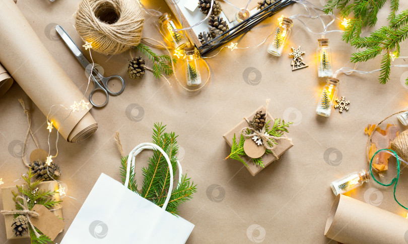 Скачать Упакуйте подарок на Рождество и новый год из экологически чистых материалов: крафт-бумаги, живых еловых веток, шишек, шпагата. Бирки с макетом, натуральный декор, ручная работа, сделай сам. Праздничное настроение. Рождественский фон фотосток Ozero