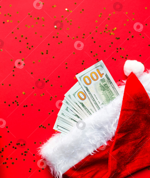 Скачать Пачка 100-долларовых купюр в шляпе Санты на красном фоне с золотыми блестками. Рождественский подарок в виде финансов, сбережений, богатства, расходов в новом году. Плоско. Инвестиции, бизнес, настоящее время. Стек в 100 долларов фотосток Ozero