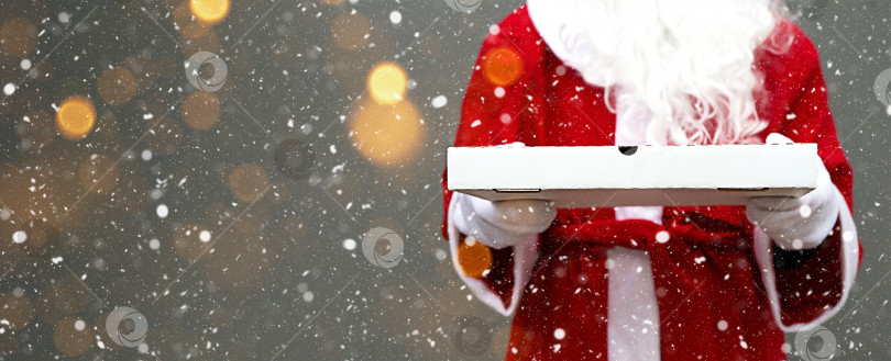 Скачать Белая коробка из-под пиццы в руках Санта-Клауса, с бородой, в красном пальто. Рождественская доставка фаст-фуда. Акция в канун Нового года. Работаем в праздничные дни в сфере общественного питания. Скопируйте пробел, сделайте макет. Баннер фотосток Ozero