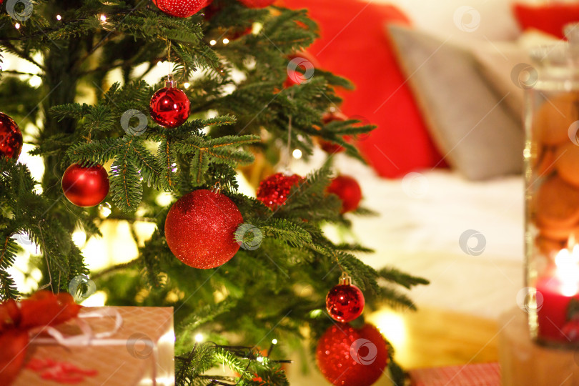 Скачать Красное рождественское украшение на рождественской елке с гирляндами огней. Новый год, элементы домашнего декора. Пространство для текста фотосток Ozero