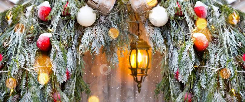 Скачать Уличные рождественские украшения из натуральных еловых веток, игрушек, гирлянд и светящегося фонаря на снегу в метель. На улице зима, снегопад. Новогодний декор фотосток Ozero