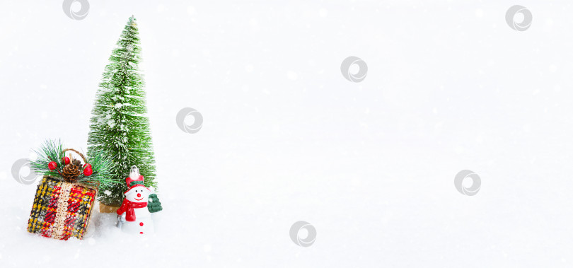 Скачать Рождественская елка, подарочная коробка и игрушечный снеговик на белом натуральном снегу во время снегопада. Украшение на Новый год и Рождество, поздравительная открытка с копировальным пространством фотосток Ozero