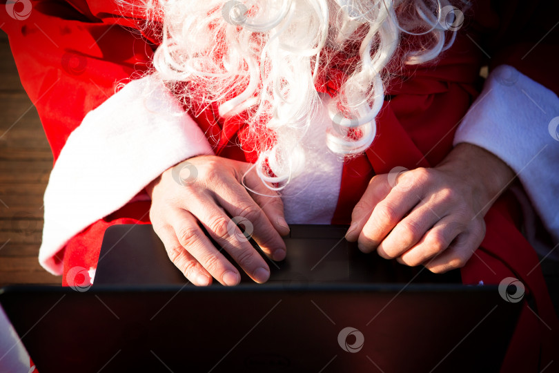 Скачать Санта-Клаус с ноутбуком и подарком в руке. Закажите подарки на Рождество и новый год через интернет-магазин. Заказ услуг аниматора на праздники. фотосток Ozero