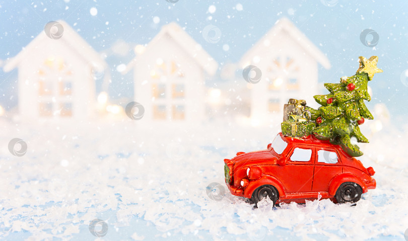 Скачать Рождественский декор - красный ретро-автомобиль на снегу проносится мимо белых домов с гирляндами огней в стиле боке, рождественская елка с подарочными коробками на крыше. Игрушка на синем фоне, место для текста. Новый год в городе фотосток Ozero