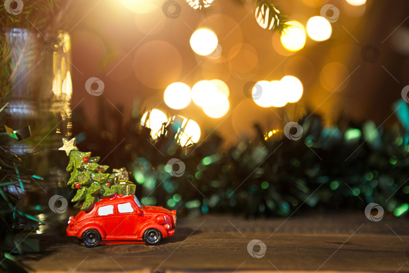 Скачать Рождественский декор - красный ретро-автомобиль везет рождественскую елку с подарочными коробками на крыше. пространство для текста. новый год. Игрушка на ветке ели с золотыми огнями гирлянд в расфокусировке, боке, праздничный фон фотосток Ozero