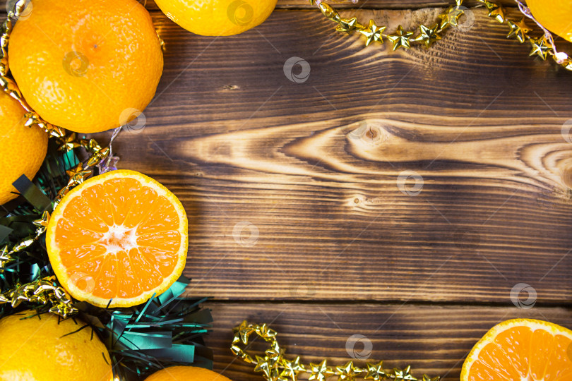 Скачать Новогодний праздничный фон из дерева с мандаринами, гирляндами и зеленой мишурой. Половинка апельсина, цитрусовый аромат праздника. Рождество, Новый год. Место для текста. Рамка фотосток Ozero
