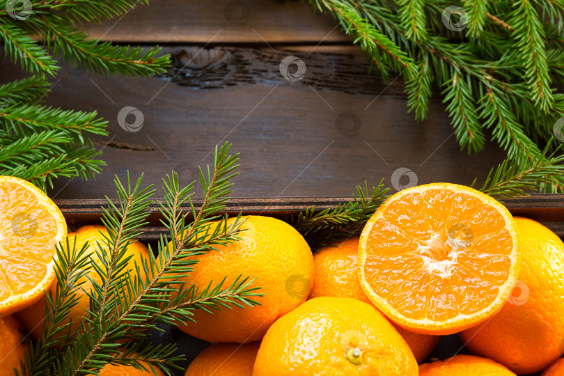 Скачать Свежие мандарины в коричневой коробке на деревянном фоне с зелеными еловыми ветками. Рамка, копировальное пространство, праздничный и зимний аромат, новый год, Рождество. Здоровая пища, апельсиновый сок, витрина магазина. Нарезать ломтиками фотосток Ozero