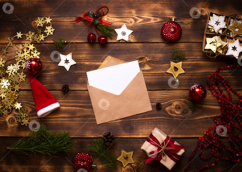 Скачать Почтовый конверт из крафт-бумаги с белым листом для текста на деревянном фоне с рождественским декором. Письмо Деду Морозу, список желаний, новогодняя мечта, подарок. Плоское расположение, пространство для копирования фотосток Ozero