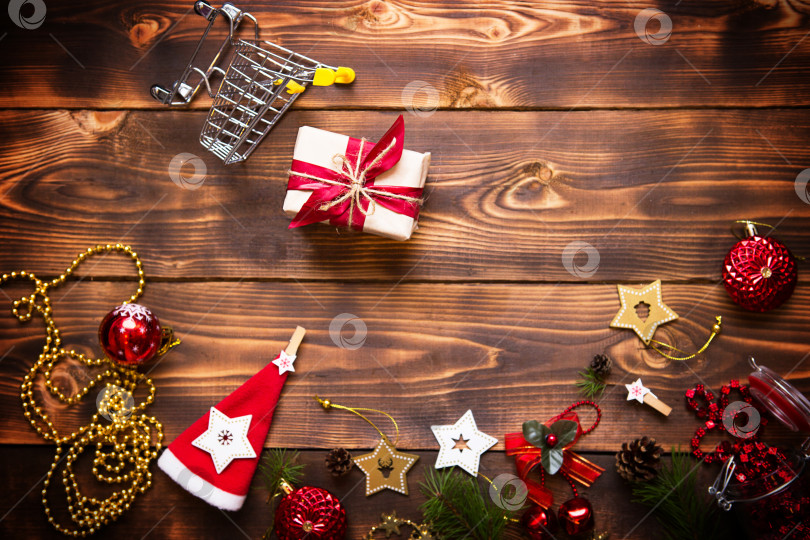 Скачать Рождественская плоская обложка на тему покупок, тележка с подарочной коробкой. Покупка подарков на новый год. Черная пятница, распродажа, декор из звезд, шара, бус, гирлянд на деревянном фоне. Пространство для текста фотосток Ozero