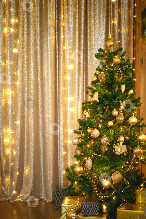 Скачать Рождественская зеленая искусственная елка в Золотой комнате с гирляндами огней, украшенная золотыми шарами, бусинами и игрушками. Коробка с подарками в фольге и черной бумаге. новый год. Пространство для текста фотосток Ozero
