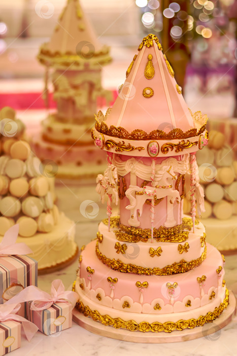 Скачать Розовый торт, богато украшенный в виде башенки с каруселью и лошадками для девочки на витрине магазина. Вертикальный. Крупный план фотосток Ozero