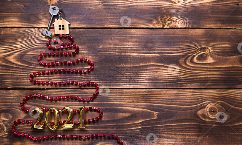 Скачать Ключ от дома с брелоком на макушке рождественской елки из красных квадратных бусин. Плоская поверхность на деревянном фоне. Строительство или покупка дома в новом году. Ипотека, аренда недвижимости. Пространство для текста фотосток Ozero