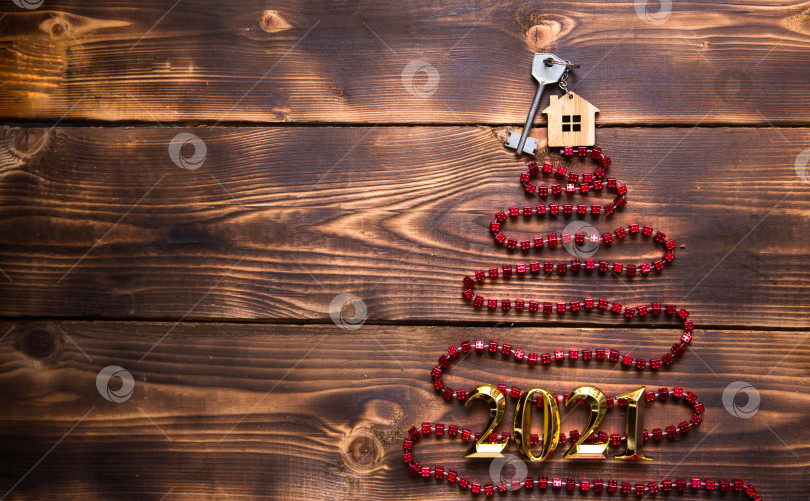 Скачать Ключ от дома с брелоком на макушке рождественской елки из красных квадратных бусин. Плоская поверхность на деревянном фоне. Строительство или покупка дома в новом году. Ипотека, аренда недвижимости. Пространство для текста фотосток Ozero