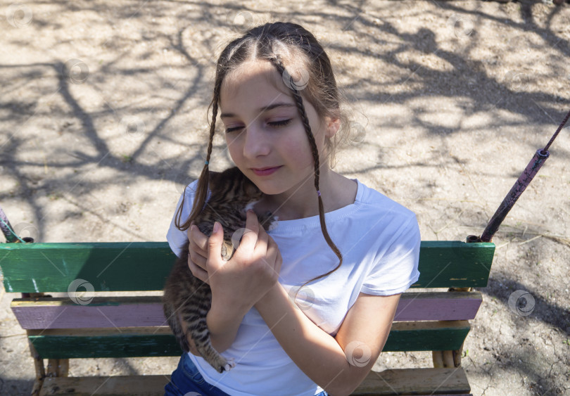 Скачать Девочка-подросток с дружелюбным лицом и закрытыми глазами нежно обнимает полосатого котенка фотосток Ozero