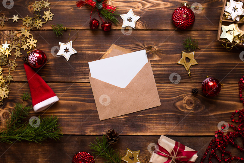 Скачать Почтовый конверт из крафт-бумаги с белым листом для текста на деревянном фоне с рождественским декором. Письмо Деду Морозу, список желаний, новогодняя мечта, подарок. Плоское расположение, пространство для копирования фотосток Ozero