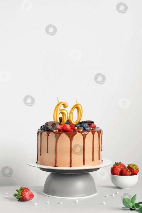 Скачать Шоколадный праздничный торт с ягодами, печеньем и числом шестьдесят золотых свечей на белом фоне, место для копирования фотосток Ozero