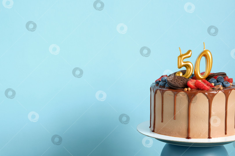 Скачать Шоколадный праздничный торт с ягодами, печеньем и пятьюдесятью золотыми свечами на синем фоне стены, место для копирования фотосток Ozero
