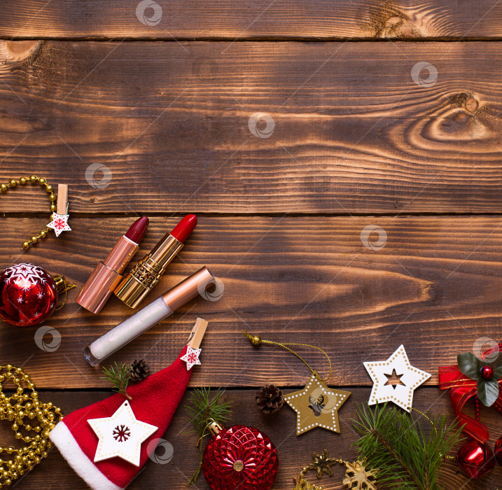 Скачать Красная помада, блеск для губ и веки на деревянном фоне в рождественском декоре. Праздничный макияж на новый год, подарок, шопинг, женские желания. Пространство для текста, ровное расположение фотосток Ozero