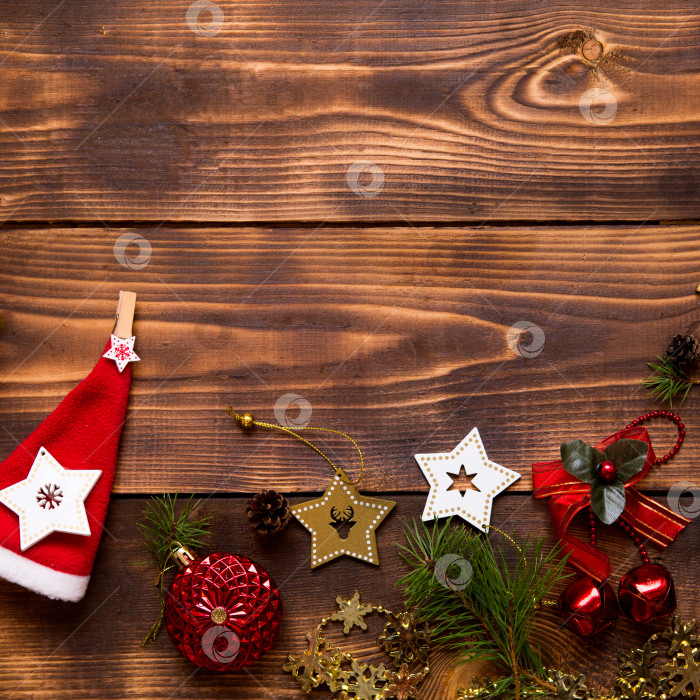 Скачать Рамка с рождественским декором на деревянном фоне. Новый год, атмосфера праздника, зеленые еловые ветки, украшения: звезды, подарочная коробка, бусы, шар, колокольчики, шишки. Пространство для текста, ровное расположение фотосток Ozero