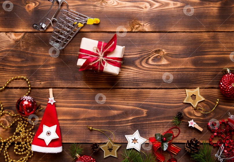 Скачать Рождественская плоская обложка на тему покупок, тележка с подарочной коробкой. Покупка подарков на новый год. Черная пятница, распродажа, декор из звезд, шара, бус, гирлянд на деревянном фоне. Пространство для текста фотосток Ozero