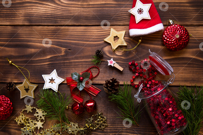 Скачать Рамка с рождественским декором на деревянном фоне. Новый год, атмосфера праздника, зеленые еловые ветки, украшения: звезды, подарочная коробка, бусы, шар, колокольчики, шишки. Пространство для текста, ровное расположение фотосток Ozero