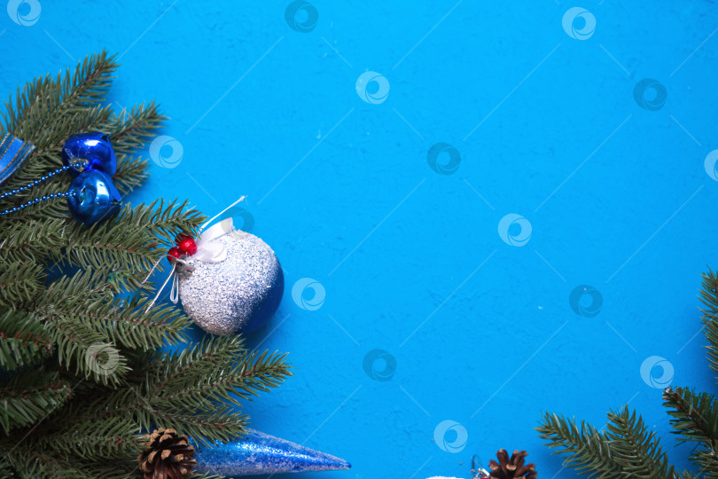 Скачать Новогодние украшения из искусственной ели, воздушные шары со снегом и ягодами, шишки, колокольчики, сосульки на синем фоне. Новый год, холодная атмосфера, мороз и лед. Рамка, пространство для текста фотосток Ozero