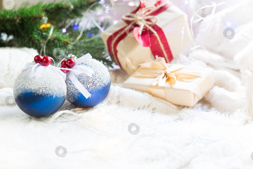 Скачать Голубые шары с искусственным снегом, рождественские подарочные коробки и украшения на белом вязаном одеяле. Новый год, праздничная атмосфера, еловая ветка, уют. Пространство для текста фотосток Ozero