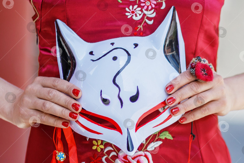 Скачать Молодая азиатская девушка прогуливается в национальной одежде с белой маской по парку. Китаянка в красном традиционном платье фотосток Ozero