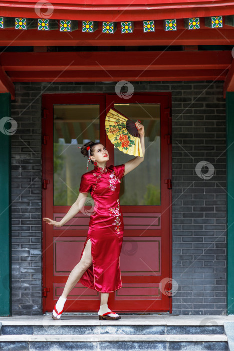 Скачать Молодая азиатская девушка прогуливается в национальной одежде с веером по парку. Китаянка в красном традиционном платье, портрет крупным планом фотосток Ozero