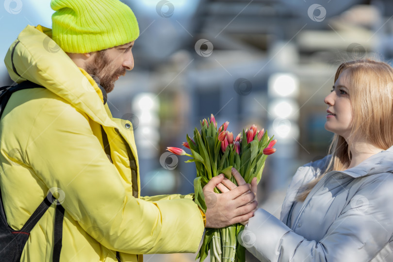 Скачать Молодая влюбленная пара на улице, держащая в руках цветы в романтический момент. Мужчина дарит красные тюльпаны блондинке.Концепция весеннего праздника - 8 марта, Пасха, Женский день фотосток Ozero