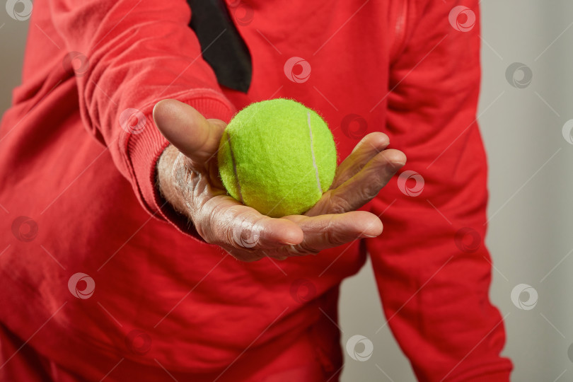 Скачать Пожилая женщина в морщинистой руке держит желтый теннисный мяч. фотосток Ozero