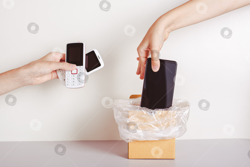 Скачать Рука выбрасывает смартфон в мусорное ведро, а вторая рука держит кнопочные телефоны фотосток Ozero