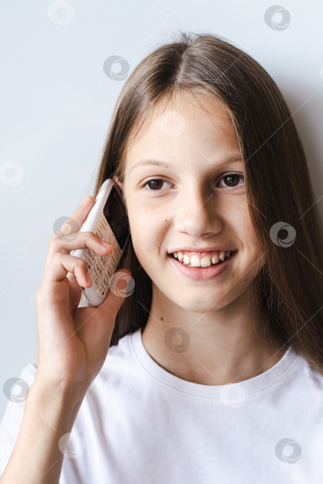 Скачать Улыбающаяся девочка-подросток разговаривает по белому кнопочному телефону вертикальный вид фотосток Ozero