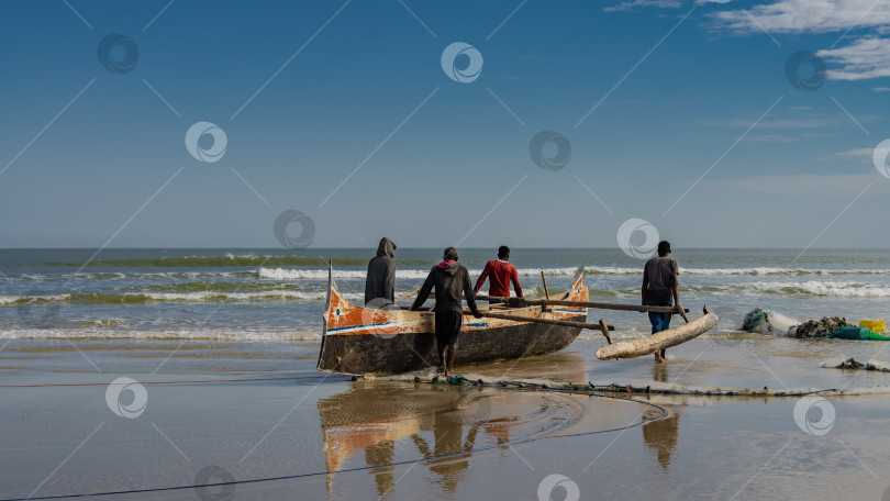 Скачать Четыре человека тащат самодельную деревянную лодку в океан. фотосток Ozero