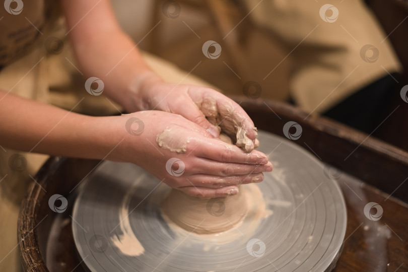 Скачать Девушка-гончар работает на гончарном круге, изготавливая керамический горшок из глины в гончарной мастерской фотосток Ozero