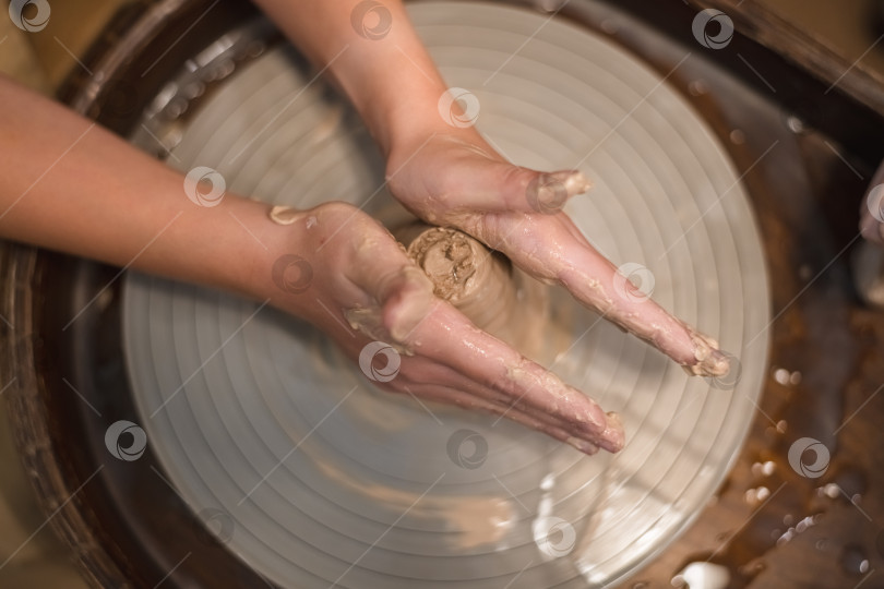 Скачать Девушка-гончар работает на гончарном круге, изготавливая керамический горшок из глины в гончарной мастерской фотосток Ozero